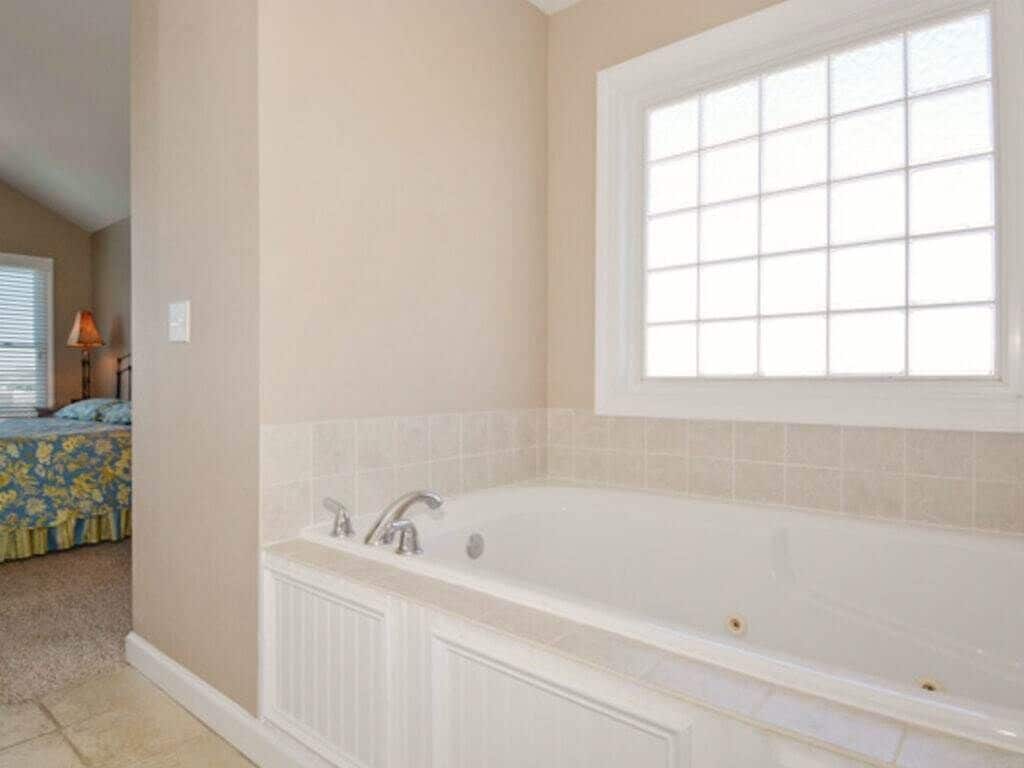 A bathroom with a large bathtub, a window above the tub, and a door leading to another room.
