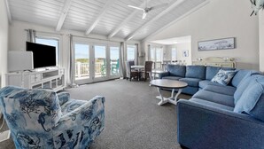 A spacious living room with a large sofa, a television, and a dining area with a table and chairs.