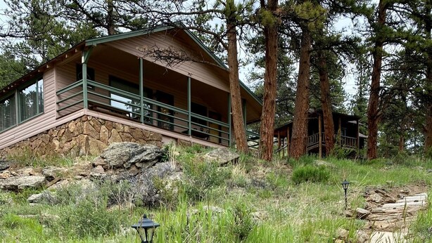 A stone staircase leading to a wooden cabin with a balcony, surrounded by grass and trees. - The Rose Den - Romantic Mountain Cabin with Views! (Estes Park)