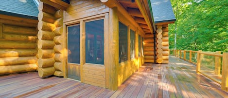 Une cabane en rondins dotée d’une terrasse en bois et de grandes fenêtres.