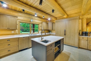 Cocina moderna con armarios de madera, una isla central con fregadero y ventana con vistas a la vegetación.