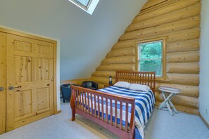 Un dormitorio tipo cabaña de madera con una cama de madera, una mesita, una silla y una ventana con persianas.