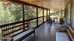 A covered porch with wooden benches and tables, surrounded by trees.