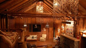 A cozy log cabin interior with a fireplace, wooden furniture, and hanging decorations.