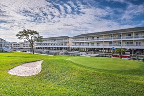 A golf course with bunkers, a water hazard, and a building with multiple balconies and a covered walkway. - Walk to Destin Beach: Coastal Condo w/ Pool Access (Destin)
