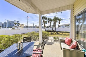 A covered outdoor seating area with a table and chairs, a lantern, and a view of palm trees and buildings in the background. - Walk to Destin Beach: Coastal Condo w/ Pool Access (Destin)