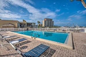 A swimming pool with lounge chairs and a fence, surrounded by buildings and palm trees. - Walk to Destin Beach: Coastal Condo w/ Pool Access (Destin)