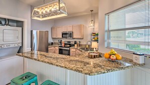 A modern kitchen with granite countertops, stainless steel appliances, and a central island with fruit. - Walk to Destin Beach: Coastal Condo w/ Pool Access (Destin)