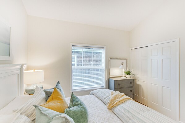 A bedroom with a bed, bedside table, lamp, window, dresser, and a door. - Steps to Beach! Airy Coastal Escape w/ Deck (Pacific Beach)