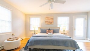A bedroom with a bed, two bedside lamps, a ceiling fan, and a large window.