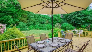 An outdoor patio with a table set for four, surrounded by chairs, under a large umbrella.