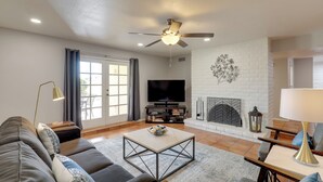 A modern living room with a sofa, coffee table, TV, fireplace, and ceiling fan. - Tucson Townhome w/ Private Patio & Mtn Views! (Tucson)