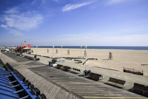 A boardwalk with benches and street lamps, leading to a sandy beach.