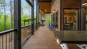 Une terrasse en bois avec une cheminée en pierre, un coin salon extérieur et une vue sur la forêt.