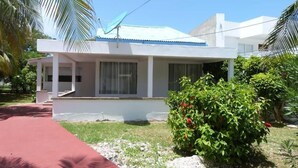 A modern two-story house with a covered porch, a satellite dish, and a well-maintained garden with a red bush and red flowers. - Casa Vacacional San Andres (San Andrés)
