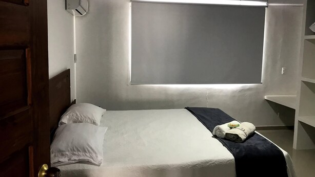 A hotel room with a bed, a window, a door, and a wall-mounted air conditioning unit. - Casa Vacacional San Andres (San Andrés)