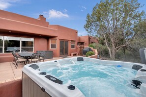 Un jacuzzi dans un jardin, avec une table et des chaises de patio, un barbecue couvert et un arbre.