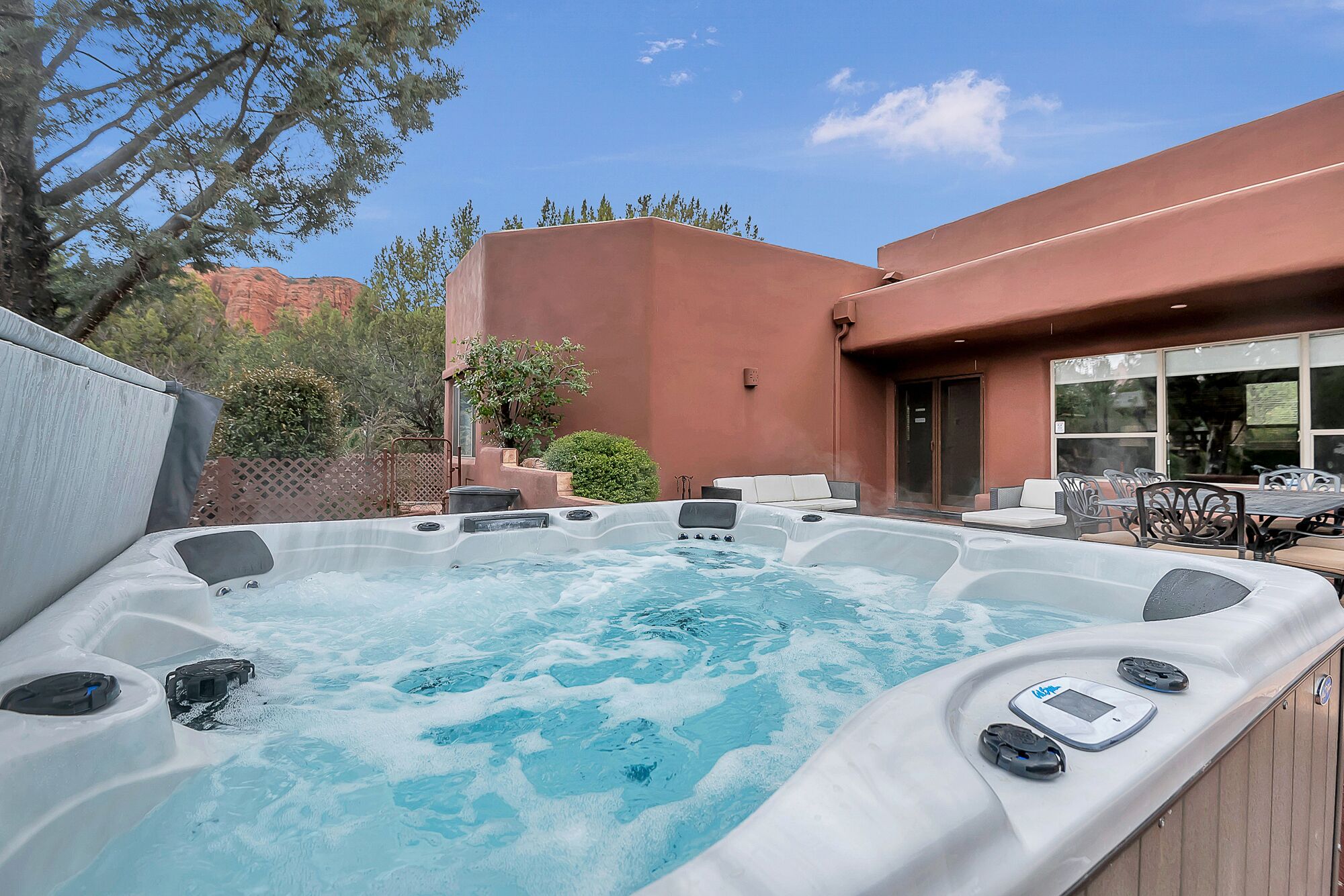 A hot tub with seating and a patio area, surrounded by a wooden deck and a building with a red exterior.