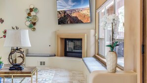 A living room with a fireplace, a large window with a view of the outdoors, a decorative wall piece, and a table with a lamp. - Discover luxury at Sedona Hidden Dream, a spacious 4BR retreat with stunning red rock views. (Sedona)