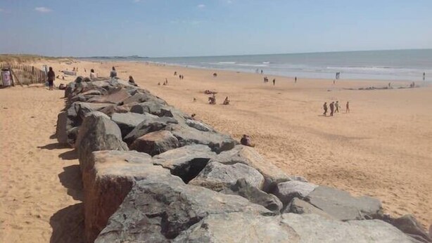 A sandy beach with large rocks in the foreground and people in the distance.