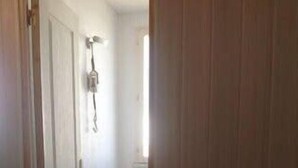 A narrow hallway with a closed door on the left and a light fixture on the wall.