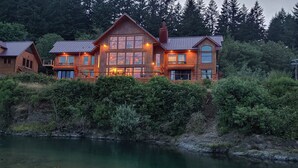 Ein großes, mehrstöckiges Holzhaus mit einem Fluss davor, umgeben von dichtem Grün.
