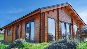 Une cabane en rondins dotée de grandes fenêtres, d’un toit en pente et d’un jardin bien entretenu.