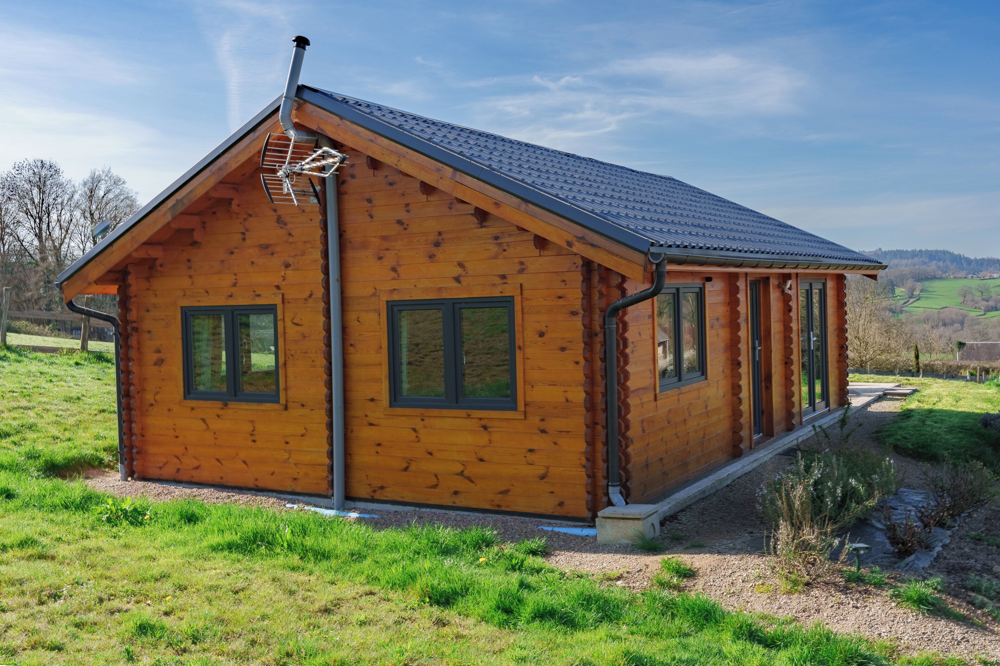 A wooden cabin with a sloped roof, large windows, and a chimney.