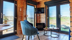 L’intérieur d’un chalet en bois, avec une grande fenêtre, un téléviseur, une cheminée et un coin repas.