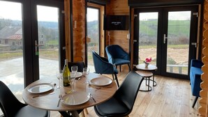 Une cabane en bois avec un coin repas comprenant une table dressée pour deux personnes, une chaise bleue et une petite table ronde sur laquelle est posée une plante en pot.