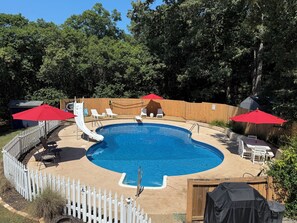 Un jardin avec une piscine, un toboggan et deux parasols rouges.