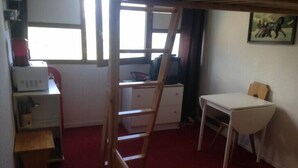 A small, compact room with a desk, a chair, a ladder, and a microwave. - Studio 3/4 fantastic view over the mountains (Le Corbier)