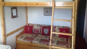A bunk bed with a lower bunk featuring a quilted mattress and red pillows, a wooden ladder, and a small framed picture on the wall. - Studio 3/4 fantastic view over the mountains (Le Corbier)