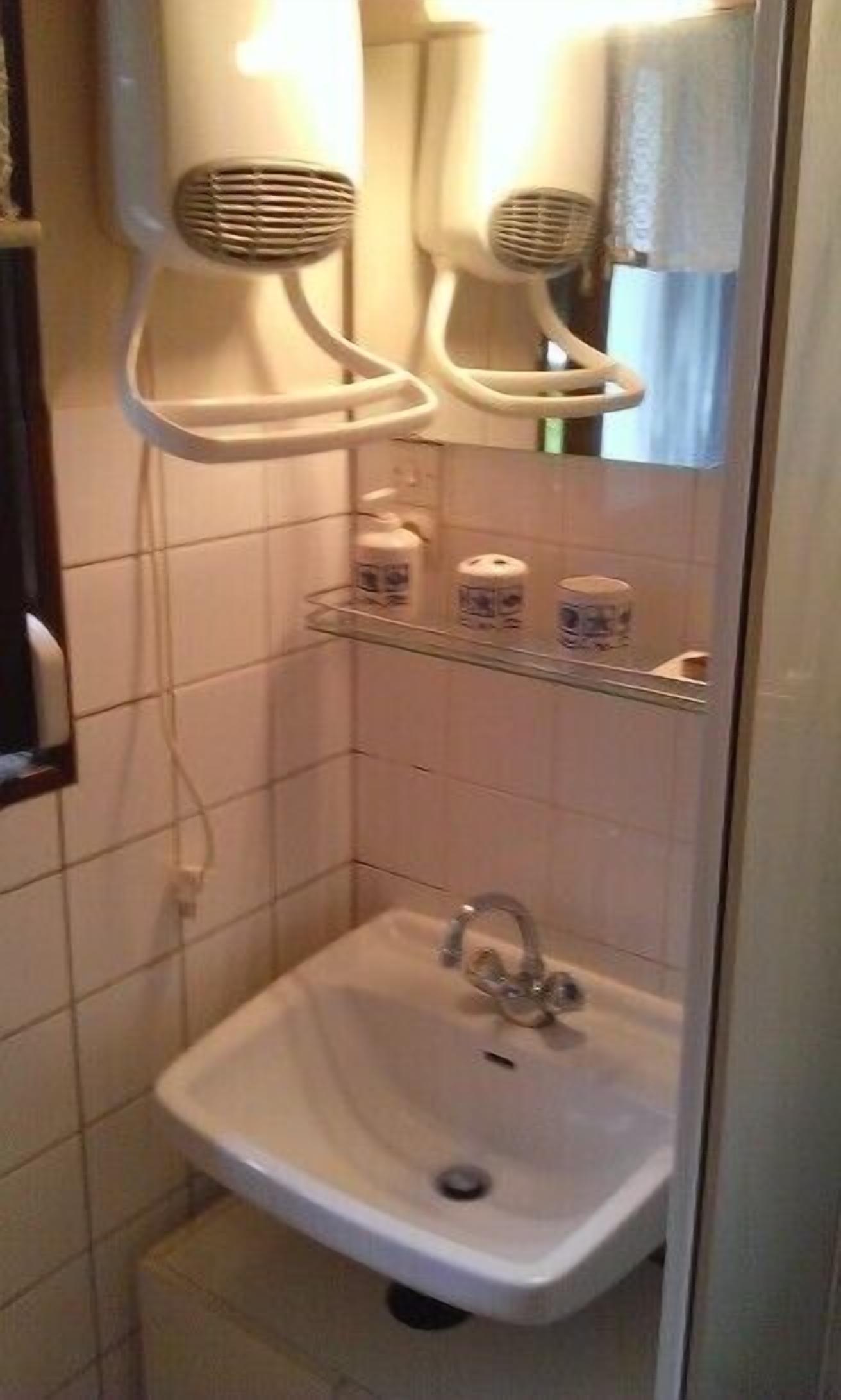 Une salle de bain avec un lavabo sur colonne, un miroir et deux sèche-cheveux fixés au mur.