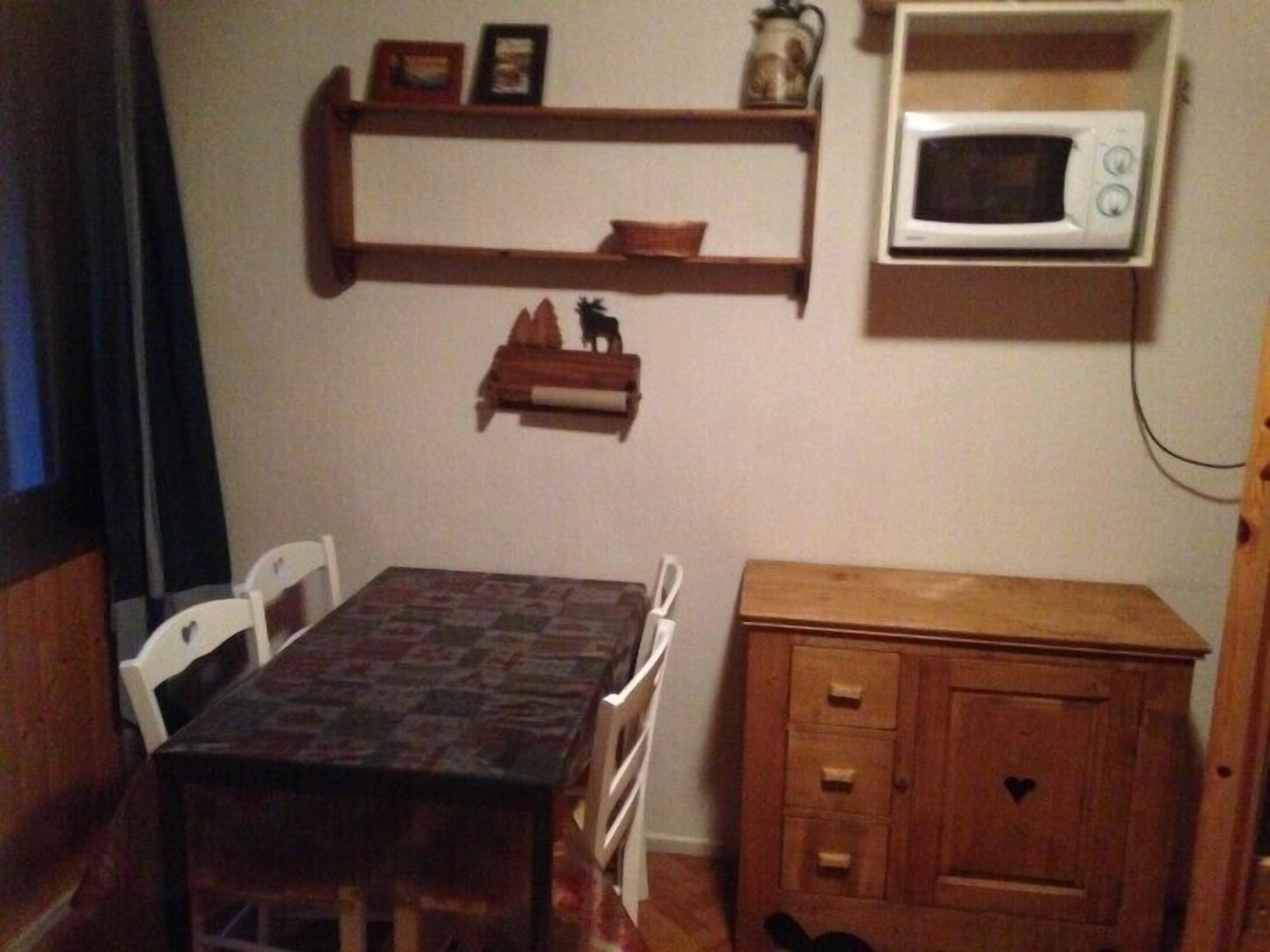 Un petit coin repas comprenant une table, des chaises, un buffet en bois et un four à micro-ondes fixé au mur.