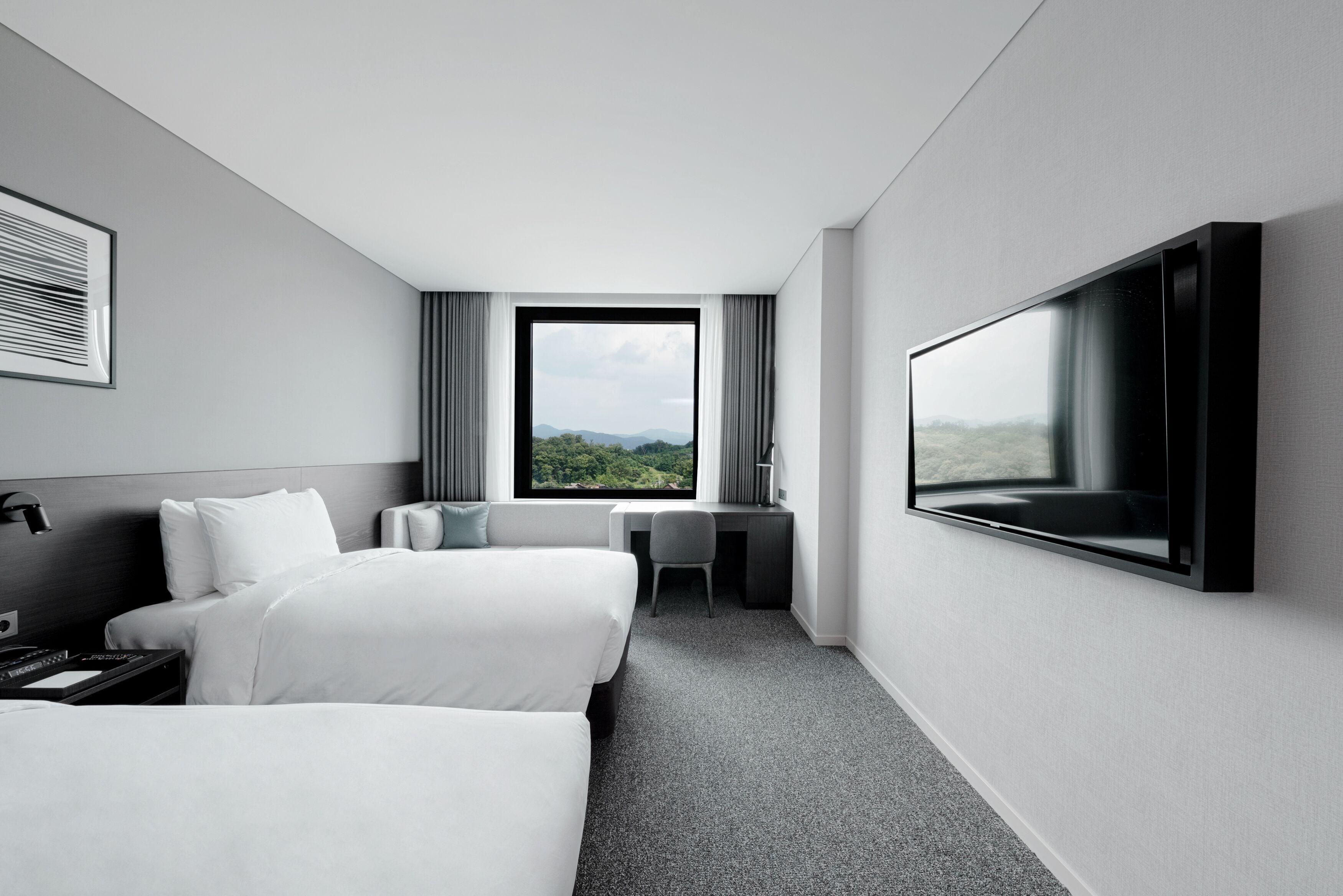 Een moderne hotelkamer met twee bedden, een bureau, een stoel, een televisie en een groot raam met uitzicht op de omgeving.