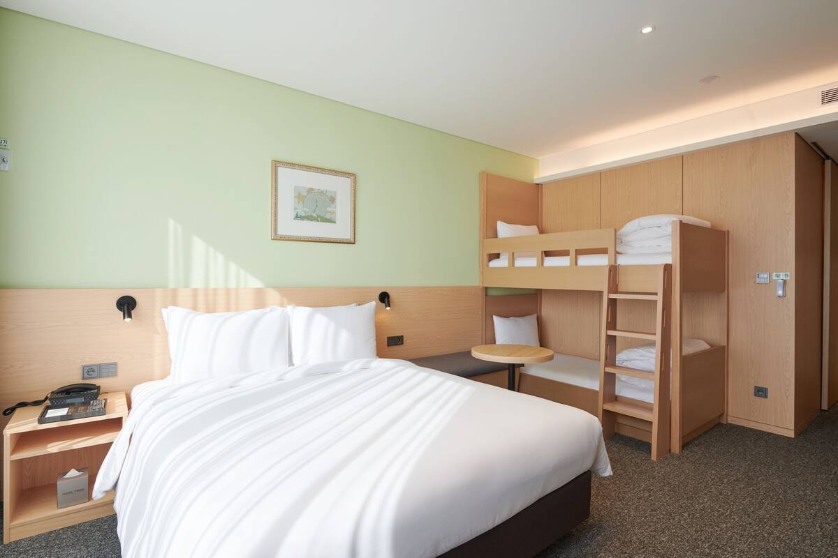 Ein Hotelzimmer mit einem großen Bett, einem Schlafstockbett, einem Nachttisch mit Telefon, einem kleinen runden Tisch und einem gerahmten Bild an der Wand.