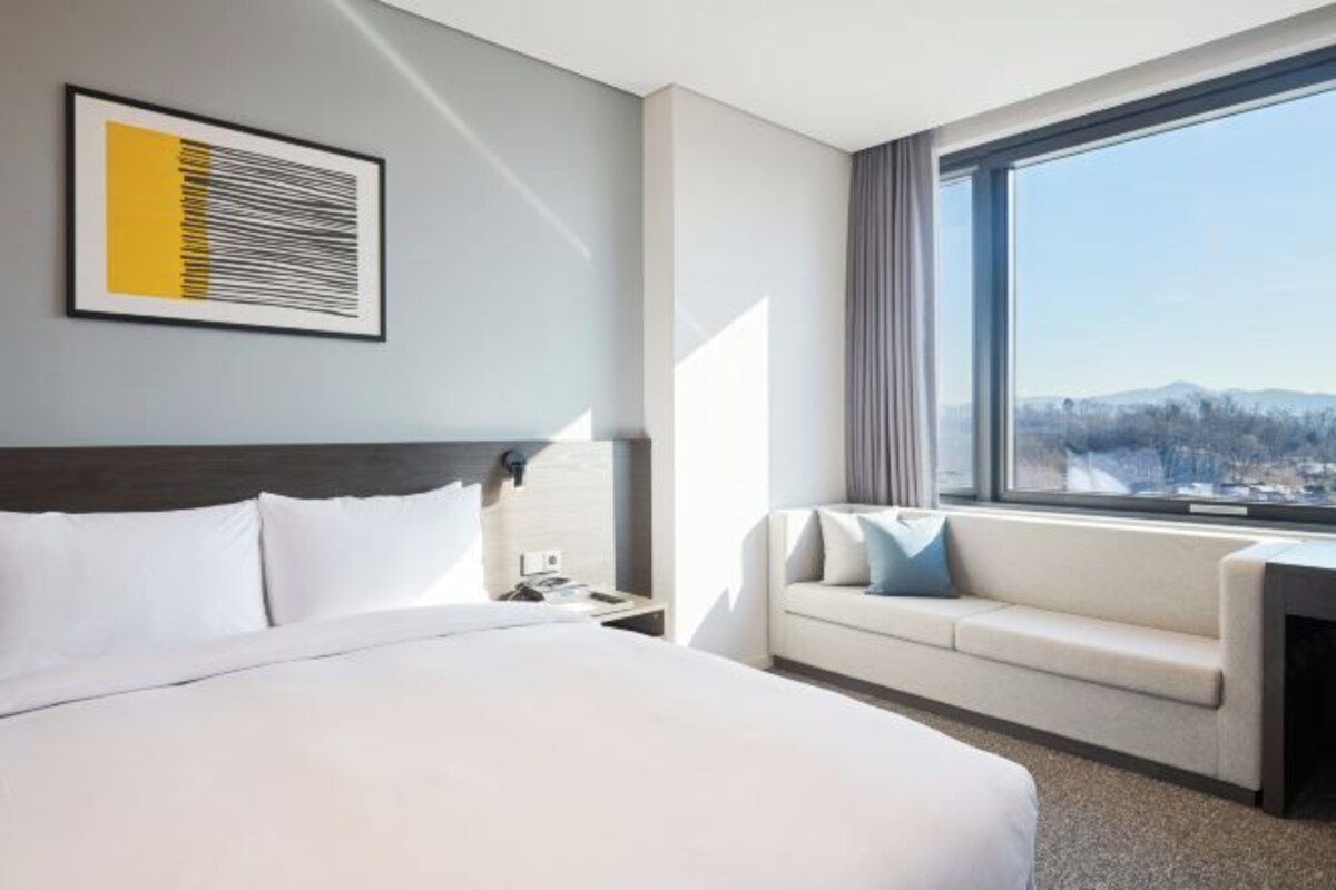 A hotel room with a large bed, a sofa, a window with a view of a snowy landscape, and a framed artwork on the wall.