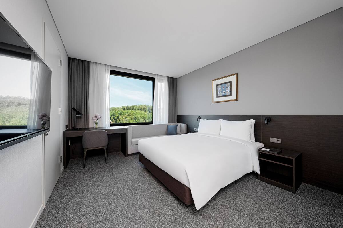 Ein modernes Hotelzimmer mit einem großen Bett, einem Schreibtisch und Blick ins Grüne.