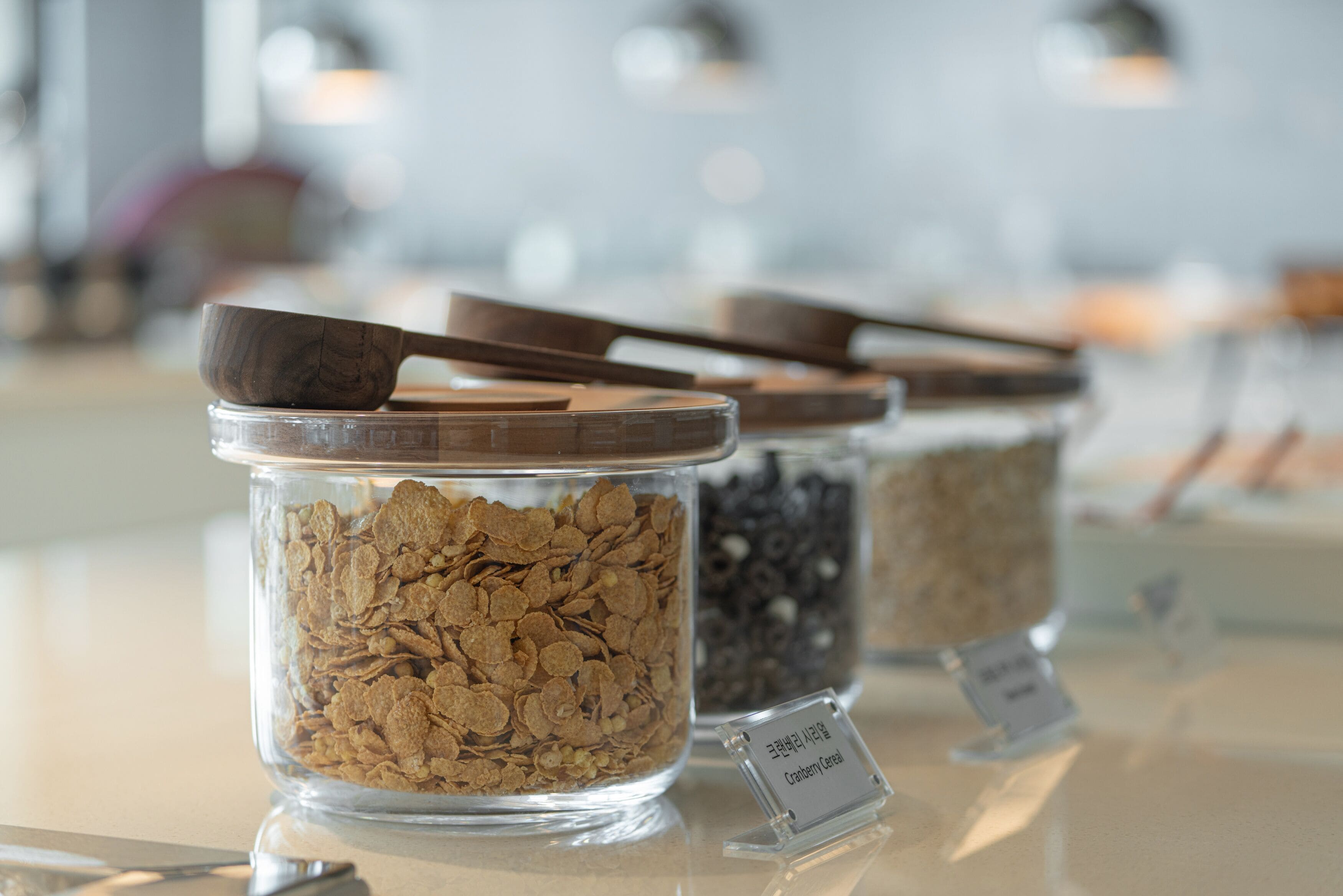 A display of cereal varieties in glass jars with wooden lids, each labeled with its name.