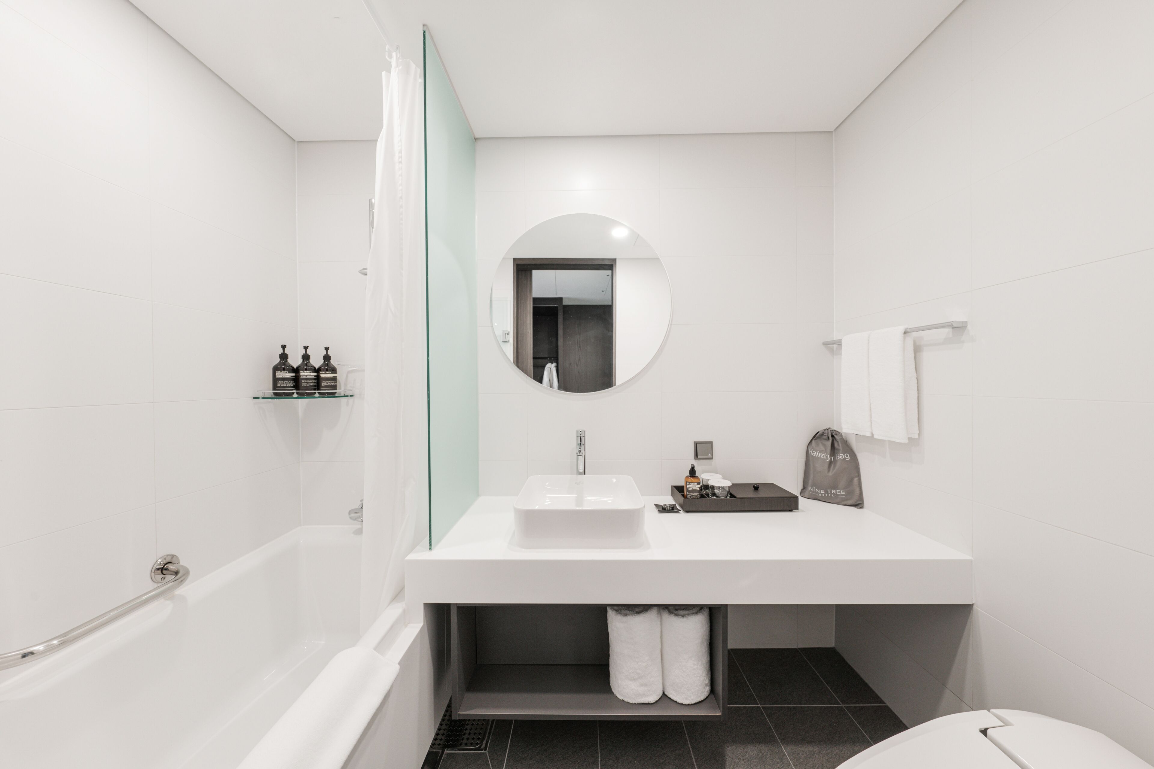 Un baño moderno con un lavamanos blanco, un espejo redondo, una bañera y una zona de ducha.