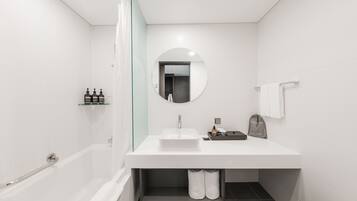 Un baño moderno con un lavamanos blanco, un espejo redondo, una bañera y una zona de ducha.