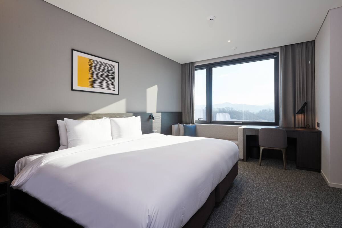 Ein Hotelzimmer mit einem großen Bett, einem Schreibtisch und Blick ins Freie.