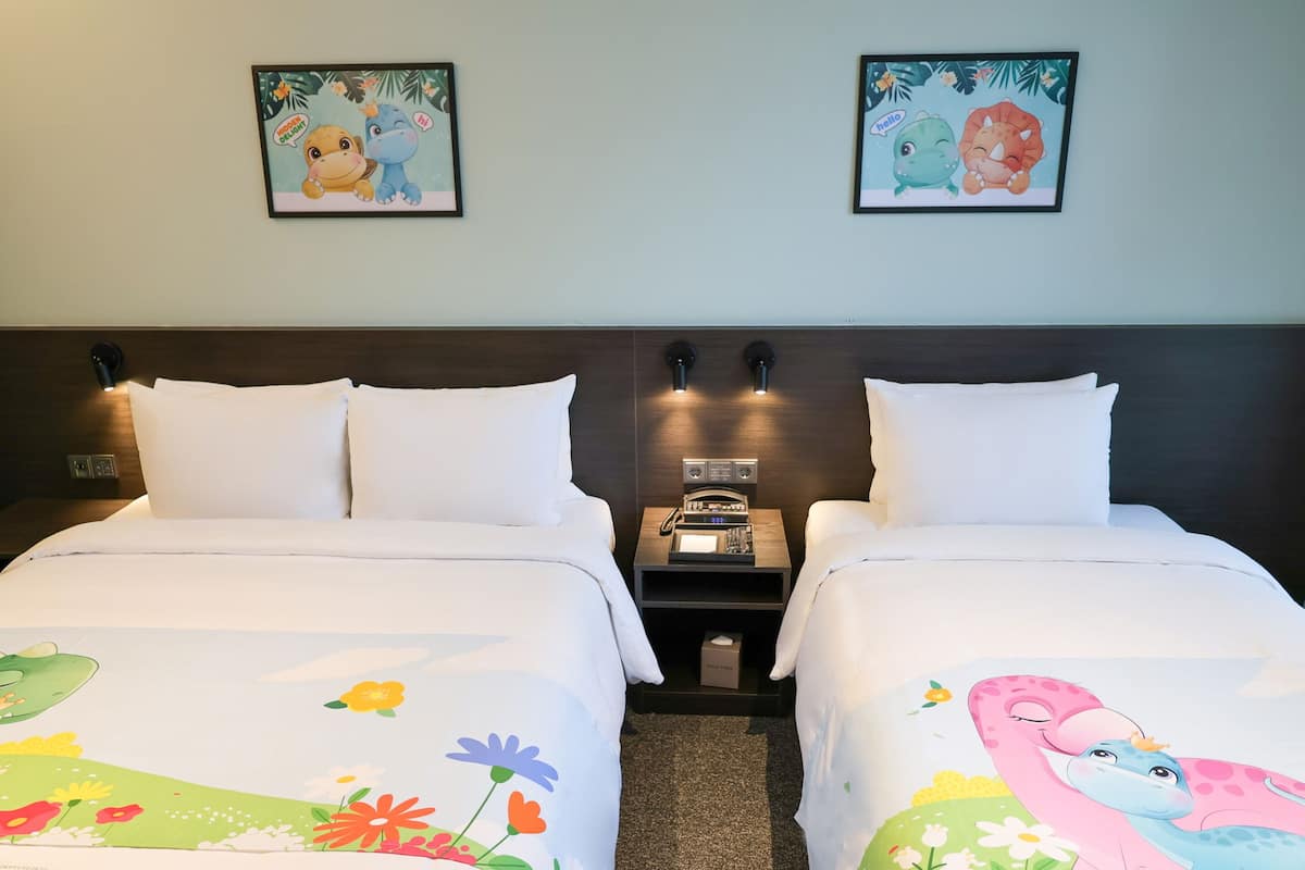 Ein Hotelzimmer mit zwei Betten, weißer Bettwäsche und Wandbildern mit Zeichentrickmotiven.