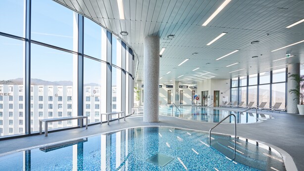 Une piscine intérieure avec des parois en verre transparent, un banc et une vue sur le paysage urbain.