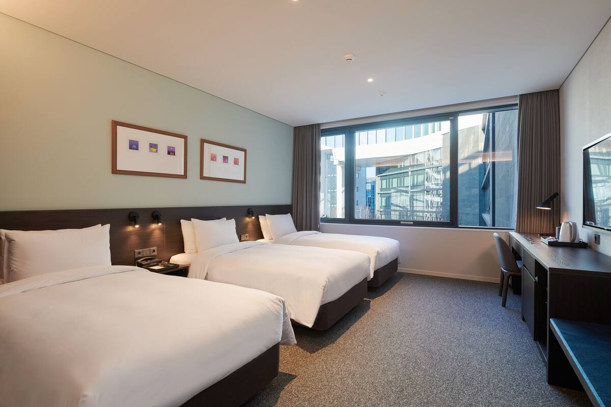 Ein Hotelzimmer mit zwei Betten, einem Schreibtisch und einem großen Fenster mit Blick auf die Stadt.
