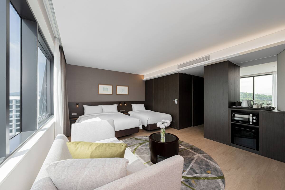 Ein modernes Hotelzimmer mit einem großen Bett, einer Couch, einem kleinen Tisch mit einer Vase und einer Küchenzeile.