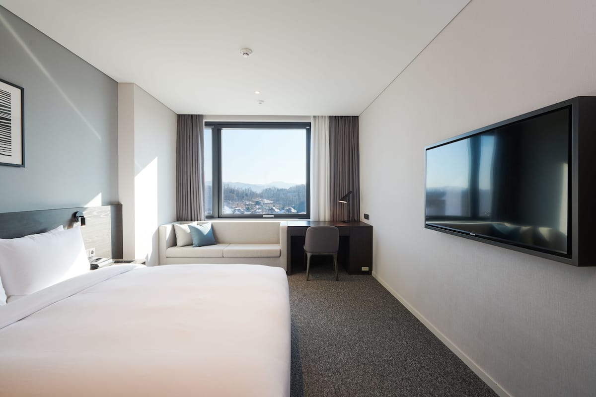 Ein modernes Hotelzimmer mit einem großen Bett, einem Schreibtisch, einem Sessel und einem Fernseher.