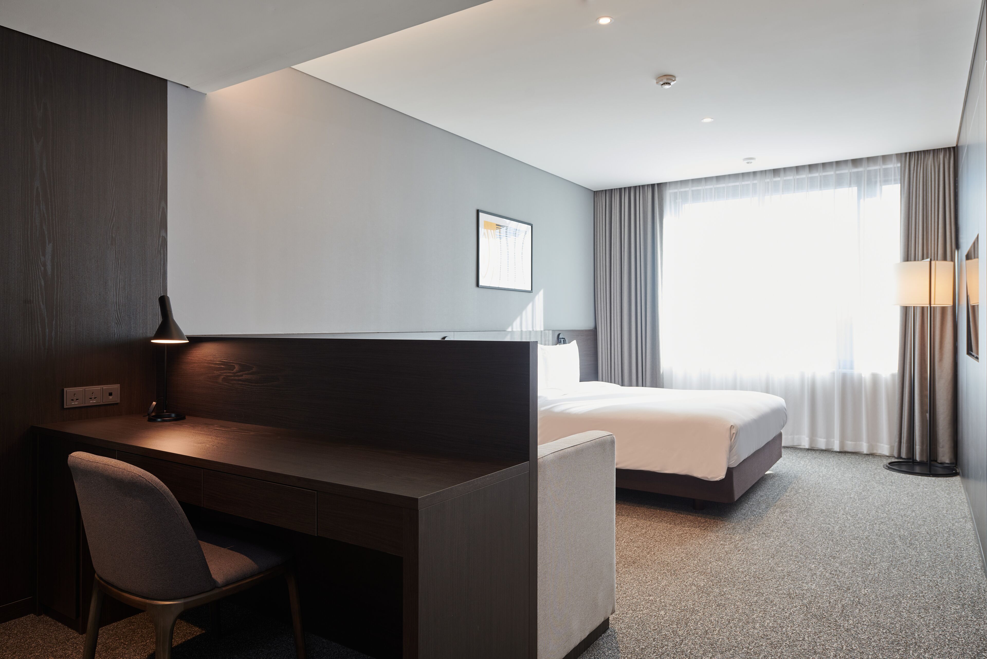 A hotel room with a desk, chair, bed, and a large window with curtains.