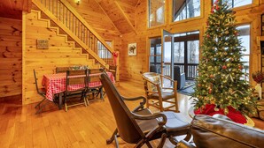 Ein gemütliches Blockhaushaus-Interieur mit einer Holztreppe, einer Essecke mit kariertem Tischläufer und einem geschmückten Weihnachtsbaum.